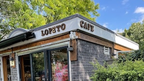 A cafe named "LOPETTO CAFE" with a brick exterior, large glass doors, and a small outdoor seating area with a table and chairs.