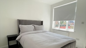 Ein Schlafzimmer mit Bett, Nachttisch und Fenster mit Jalousien.