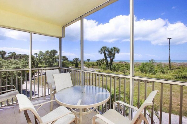 Un balcone con tavolo e sedie in vetro, con vista su una spiaggia e palme.