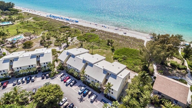 Luchtbeeld van een kusthotel met strand, parkeerplaats en zwembad.