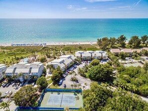 Vista aerea di un hotel sulla costa con diversi edifici, una spiaggia e un campo da tennis.