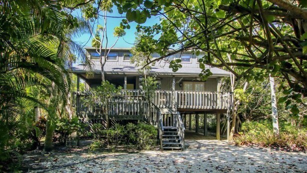 Une propriété située en bord de mer, dotée d’une terrasse en bois, d’un escalier menant à une zone abritée et d’une végétation tropicale luxuriante.