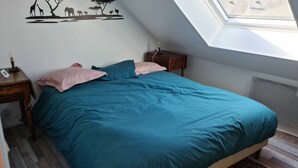 A bedroom with a sloped ceiling, a bed with teal bedding, a nightstand, a wall mural, and a view through a skylight.