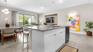 A modern kitchen with a central island, a dining area with chairs, a large window, and a painting on the wall. - 4 BD/ 4 BA/ Formosa Valley (7973 FV) (Kissimmee)
