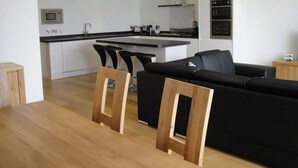 Eine moderne Küche mit weißen Schränken, einer schwarzen Arbeitsplatte und einem eingebauten Backofen. Es gibt ein schwarzes Sofa und einen Holzessttisch mit Stühlen.