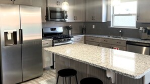 Una cocina moderna con electrodomésticos de acero inoxidable, encimeras de granito e iluminación colgante.