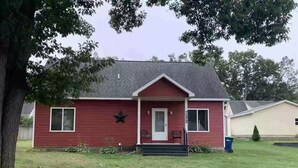 Une maison rouge à un étage, avec un porche à l’avant, un petit jardin et une boîte aux lettres.