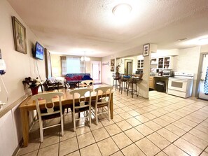 Un comedor con mesa y sillas de madera, una cocina equipada y una sala de estar con sofá y televisor.