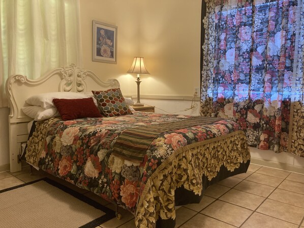 A bedroom with a floral bedspread, a white ornate headboard, a bedside lamp, and a floral curtain. - 3BR Home • 1 Mile to I-95 • Large Parking (Kingsland)