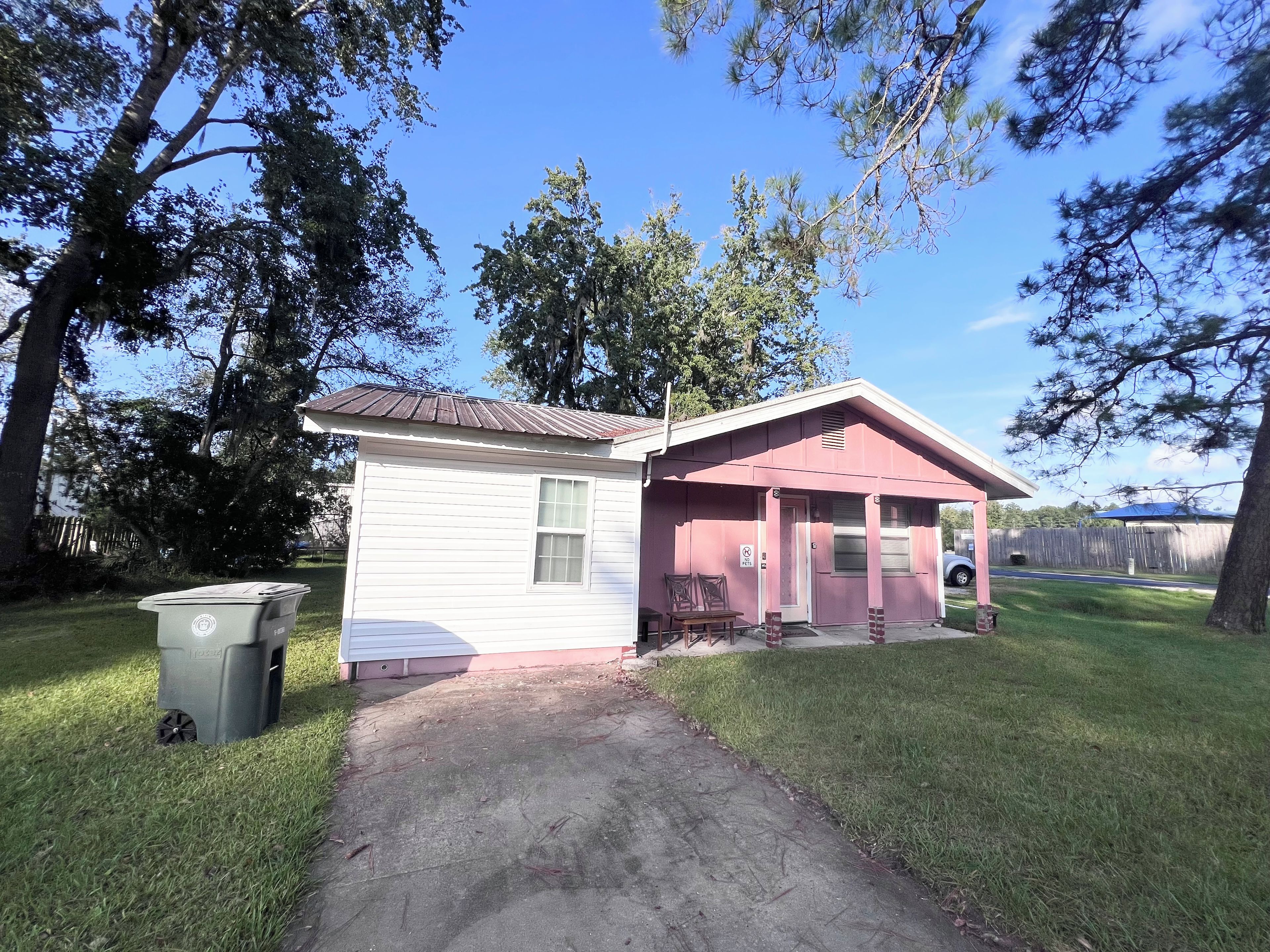 A small single-story house with a red roof and a white exterior. There is a paved driveway leading to the front door.