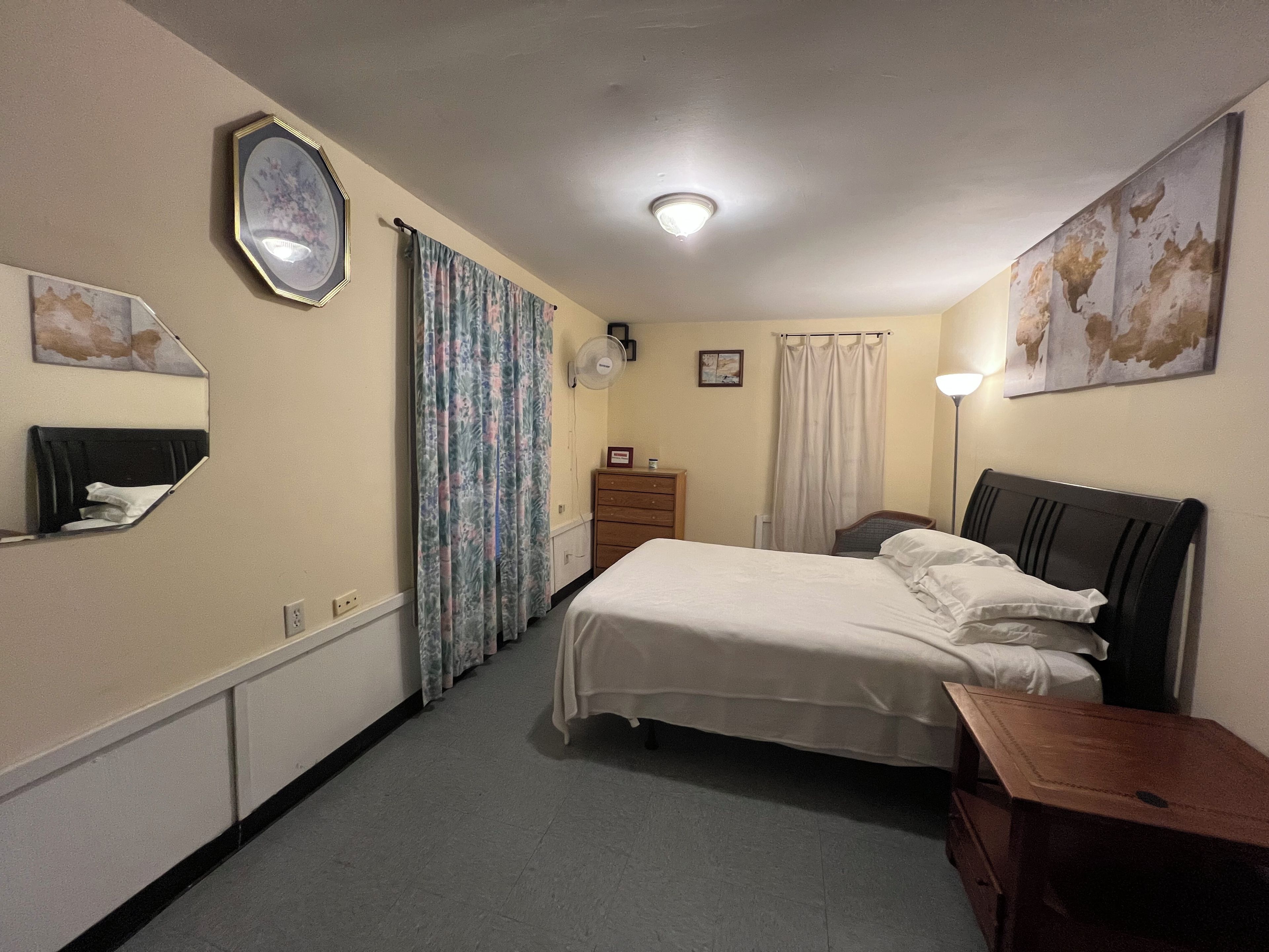 A hotel room with a bed, a dresser, a nightstand, a mirror, a lamp, and a world map on the wall.