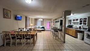 Un amplio espacio de sala con una mesa de comedor, sillas, un sofá y un televisor. La cocina cuenta con un microondas, horno y lavaplatos.