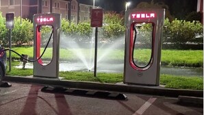 Dos estaciones de carga Tesla de noche, con un edificio y follaje al fondo.