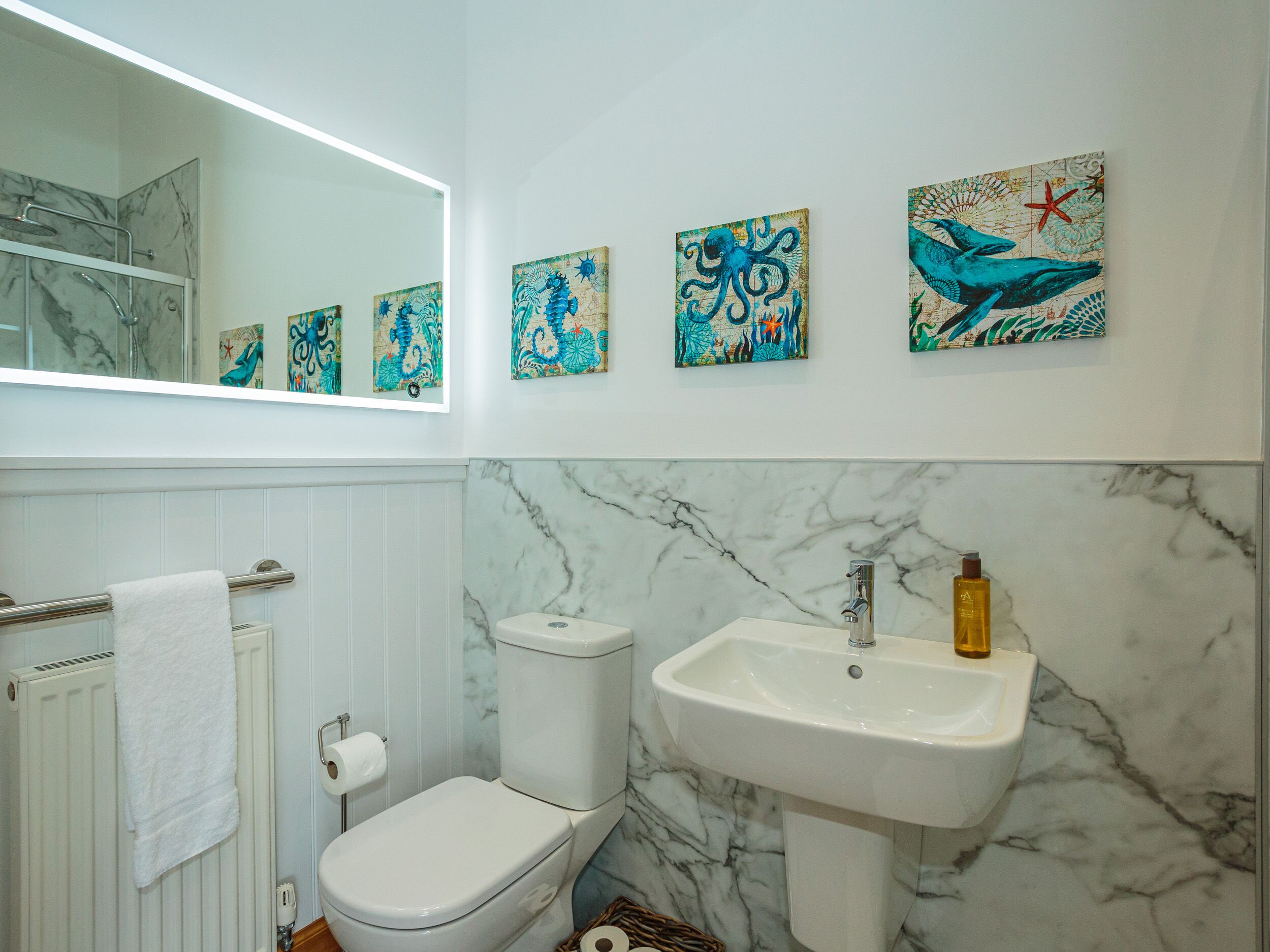 A bathroom with a toilet, sink, and a towel rack. There are four wall-mounted paintings above the sink.