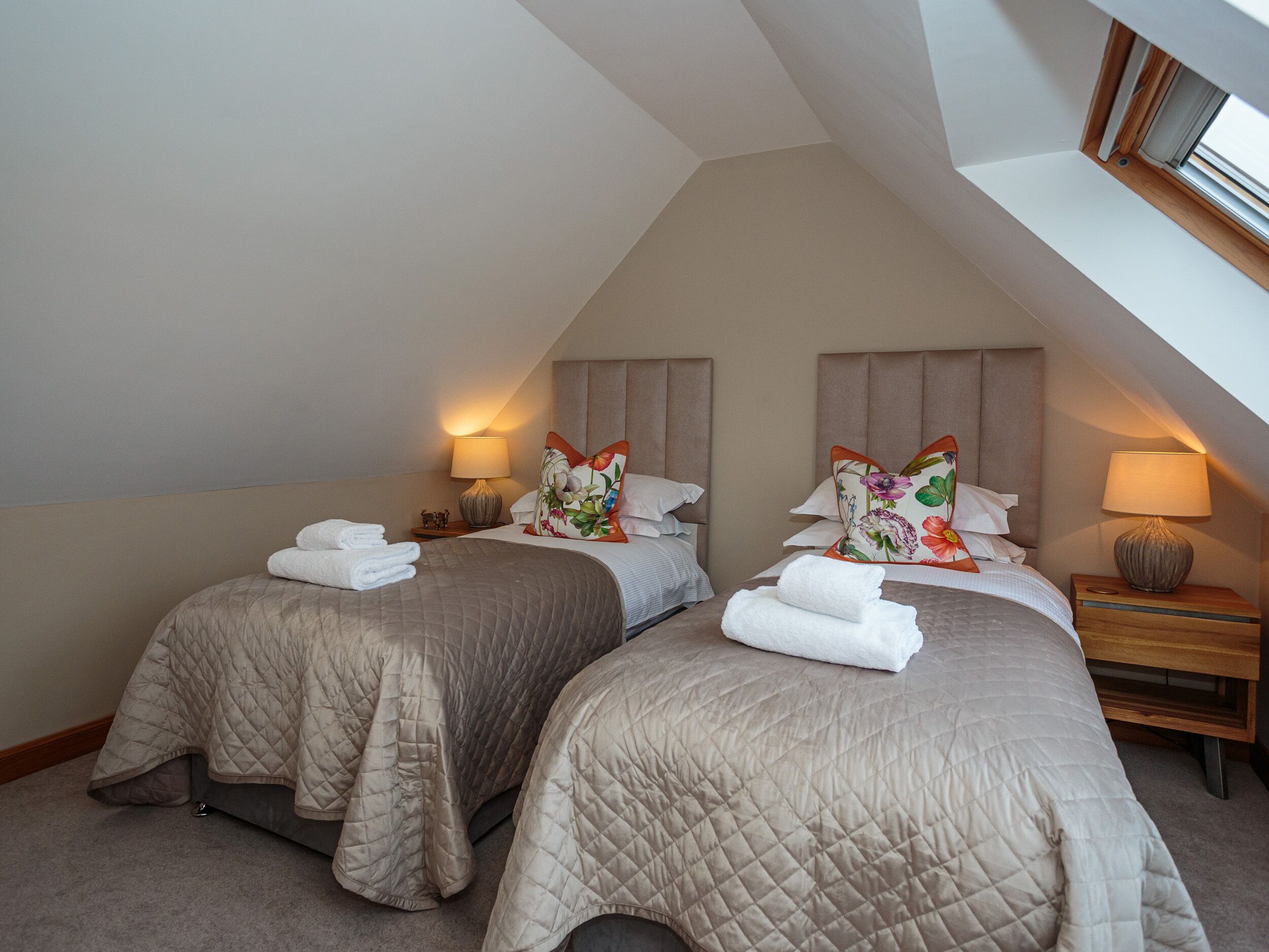 A bedroom with two beds, each with a quilted bedspread and pillows, and bedside lamps.