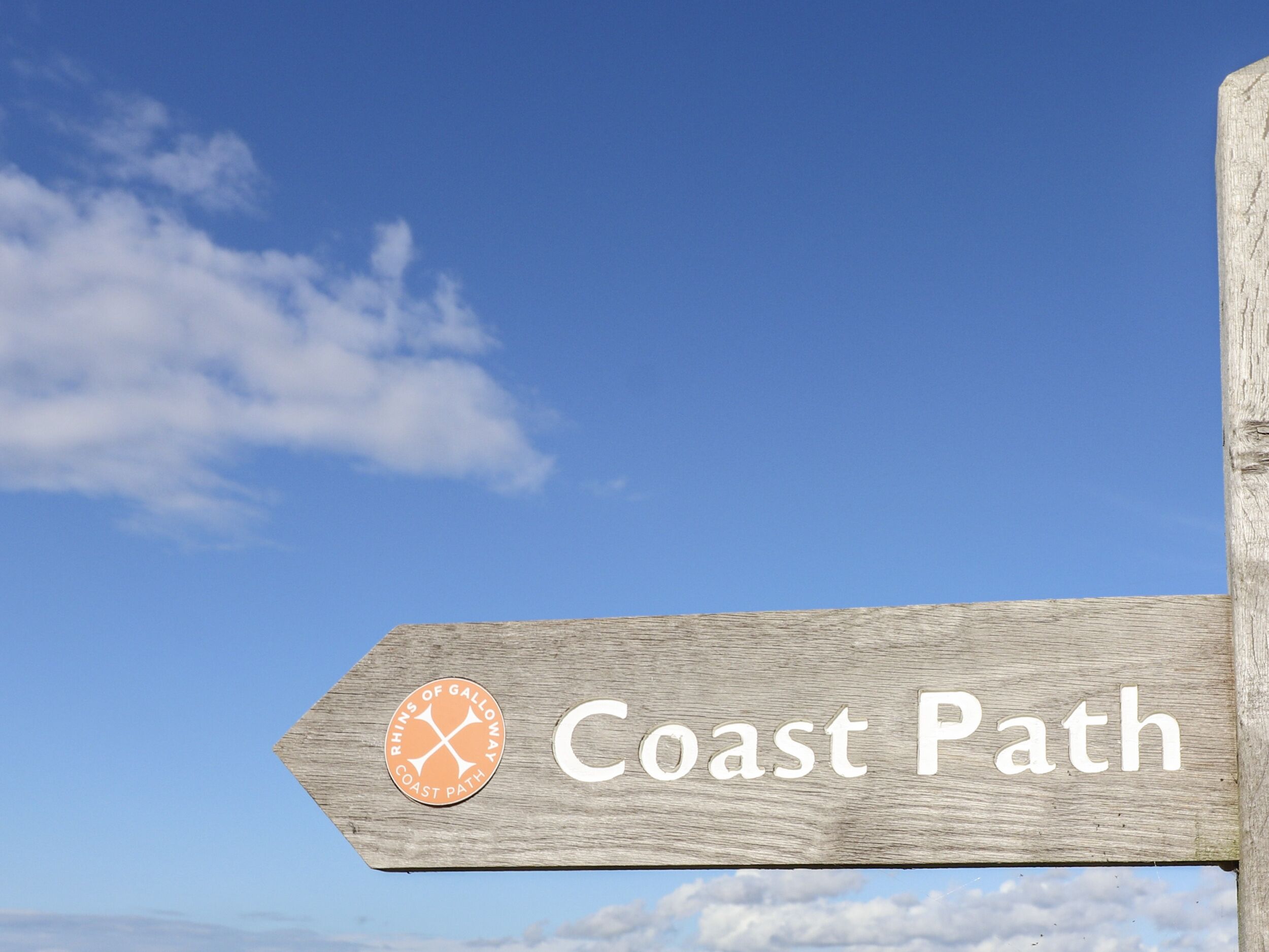 A wooden sign with the text "Coast Path" and a logo.