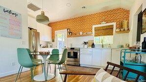 A modern kitchen with white cabinets, a built-in oven, and a dining area with a green table and chairs. - Renovated Retro Bungalow - Walk to Downtown! (Prescott)