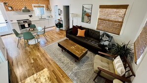A modern living room with a black leather sofa, a wooden coffee table, and a dining area with a glass table and chairs. - Renovated Retro Bungalow - Walk to Downtown! (Prescott)