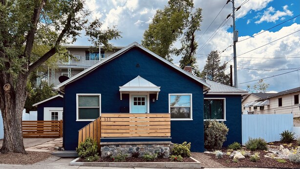 A two-story house with a dark blue exterior, a front porch with wooden steps, and a small garden area with various plants and rocks. - Renovated Retro Bungalow - Walk to Downtown! (Prescott)