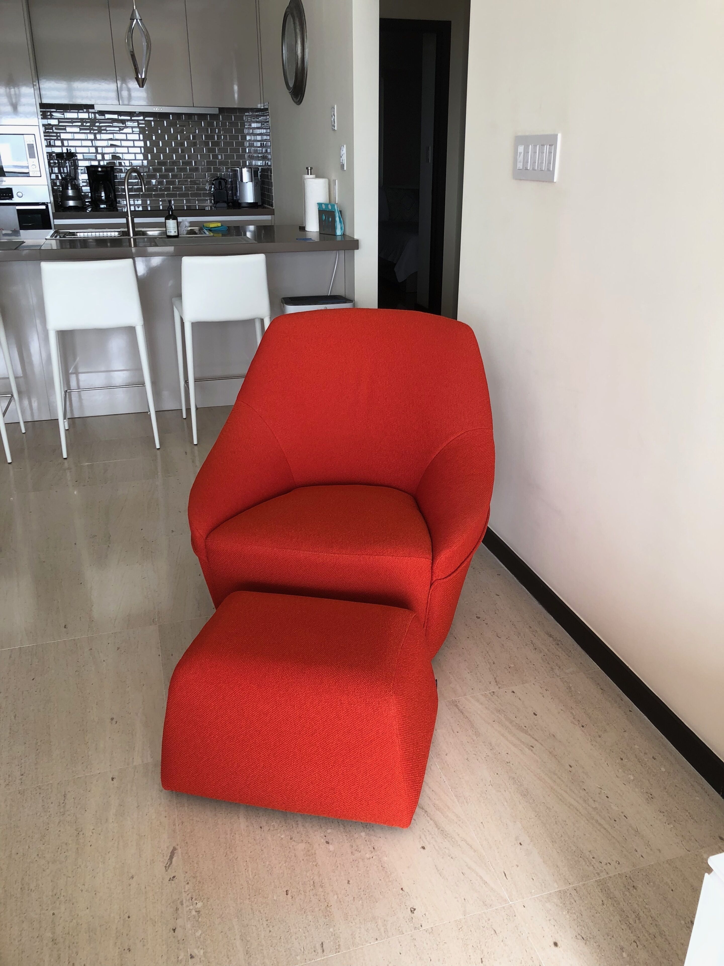 Une cuisine moderne avec un plan de travail en acier inoxydable, des chaises blanches et un fauteuil rouge.