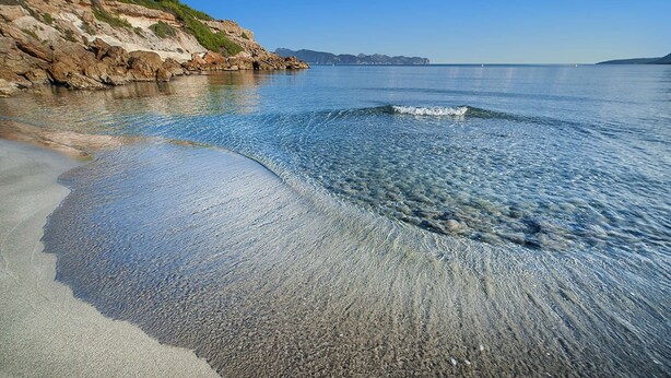 A beach with clear water, a rocky shoreline, and distant mountains. - Seafront Villa Sunset Alcudia by Balearic Villas (Alcúdia)