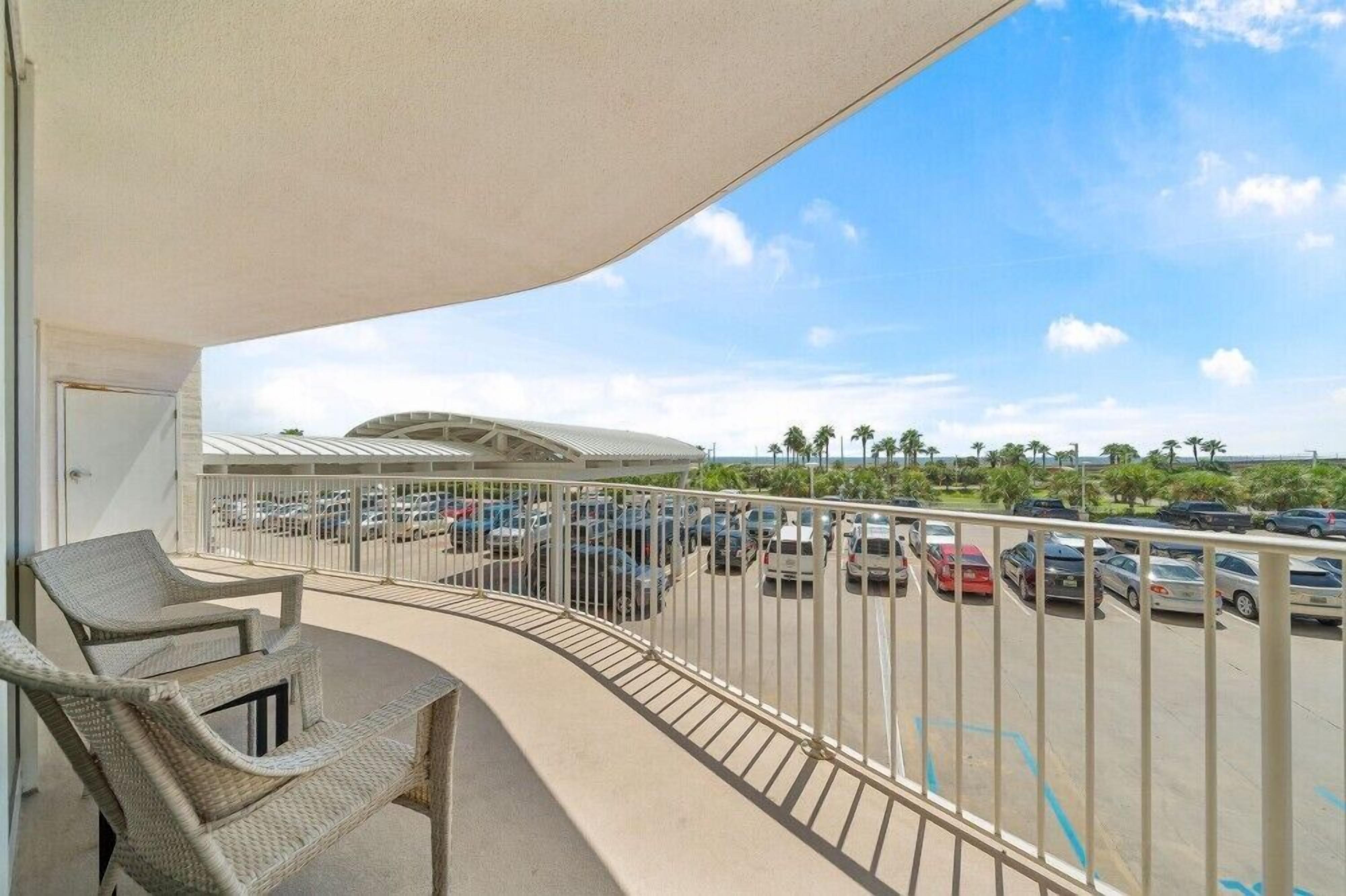 A balcony with wicker furniture, a view of a parking lot, and a building with a curved roof.