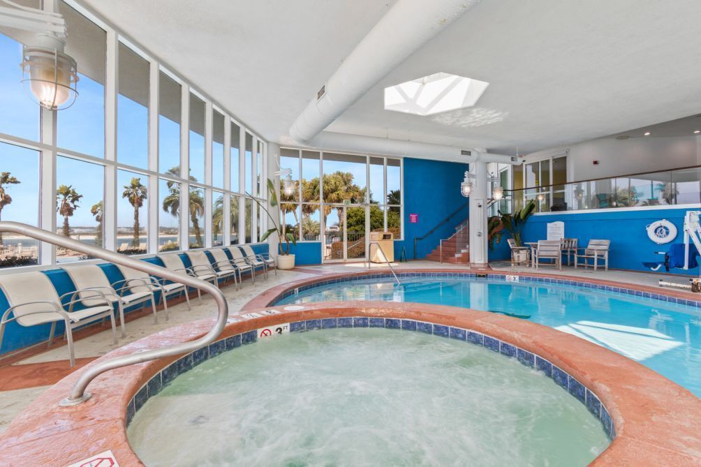 An indoor pool with clear views of palm trees outside, lounge chairs, and a blue accent wall.