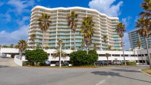 Um hotel com várias andares, fachada curva, inúmeras varandas e palmeiras.