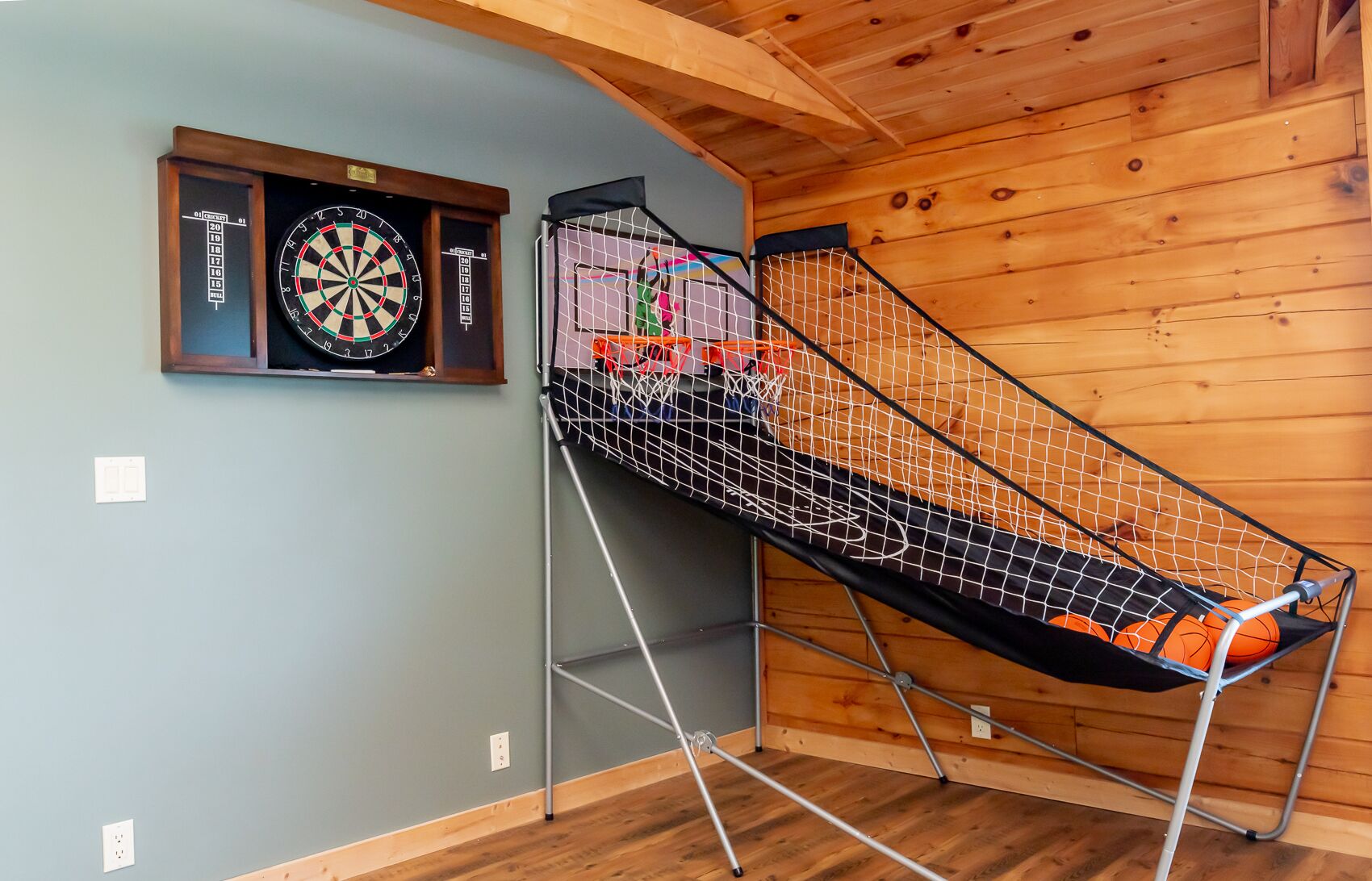 Ein Zimmer mit Dartscheibe, Basketballkorb und Holzbalkendecke.