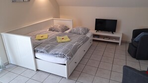 Een kleine slaapkamer met een bed, een televisie en een zithoekje.