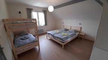 A room with a bunk bed, a single bed, a bedside table, a window with curtains, and a ceiling light.