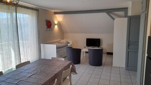Een kleine kamer met een bed, een televisie, een eettafel en een kitchenette.