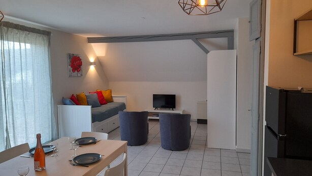 Een moderne woonkamer met een bank, televisie en een eethoek met een tafel gedekt voor twee personen.