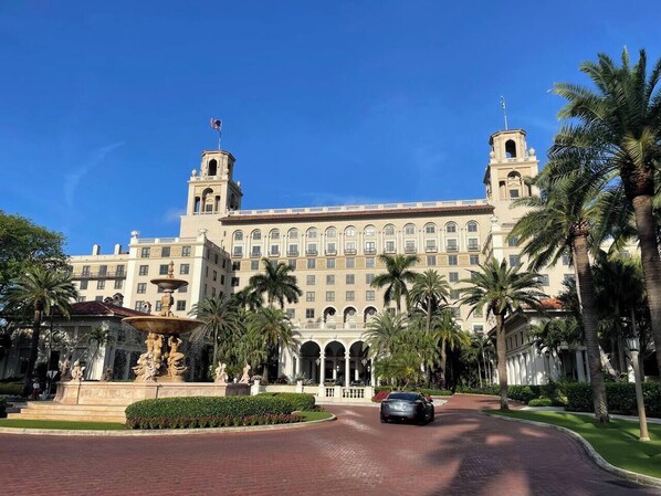 A large hotel with a central fountain, palm trees, and a clear blue sky.