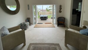 A spacious living room with a large mirror, a sofa, a chair, and a view of the backyard through a sliding glass door. - Hot tub, tiki bar, outdoor shower, water access! (West Palm Beach)
