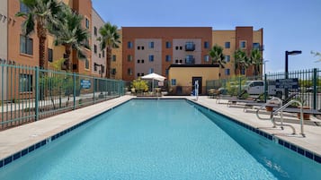 A swimming pool with a blue tiled edge, surrounded by a metal fence, and adjacent to a multi-story building with balconies.