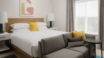 A hotel room with a bed, a grey sofa, a small table, and a window with curtains.