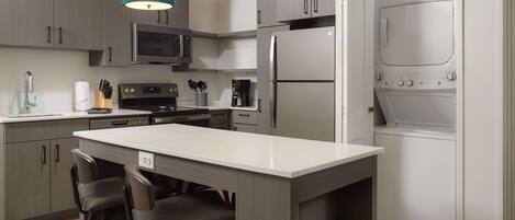 A modern kitchen with grey cabinets, a central island with bar stools, a microwave, a coffee maker, and a built-in oven.