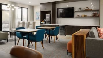 A modern hotel room with a dining area, a sofa, and a TV mounted on the wall.