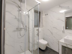 A modern bathroom with a glass-enclosed shower, a white toilet, and a marble-tiled wall.