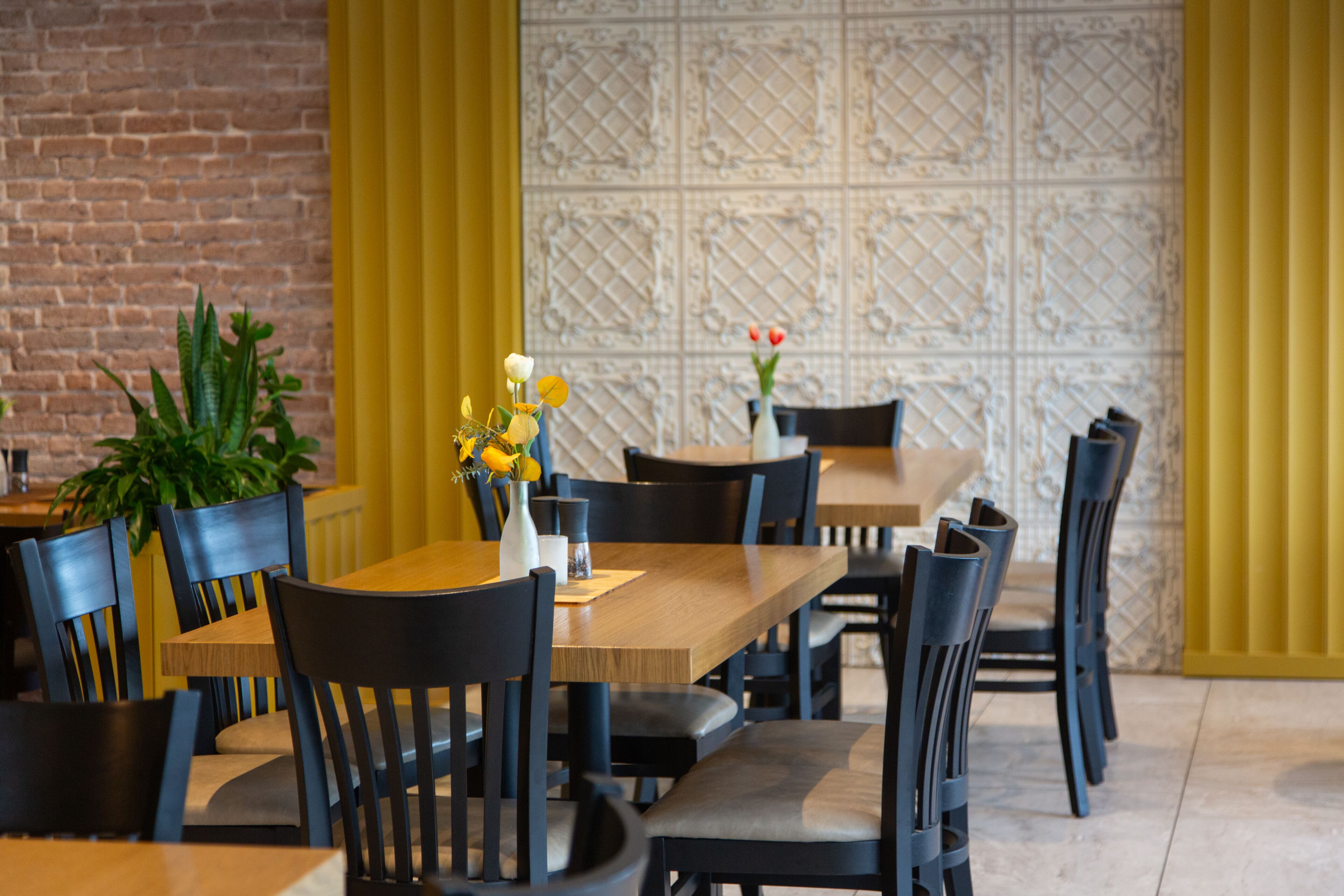 Interior de restaurante con paredes de ladrillo, cortinas amarillas y un papel tapiz estampado al fondo.