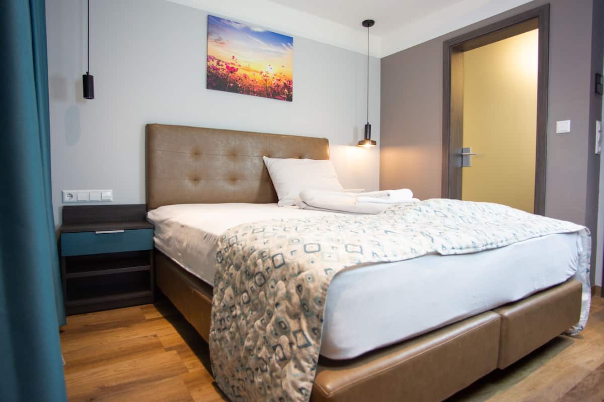 A modern hotel room with a large bed, a bedside table, a nightstand, a wall-mounted artwork, and a door.