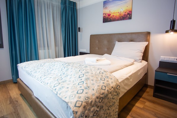 A neatly made bed with a patterned bedspread, a headboard, and a bedside table with a lamp. - ASD Hotel (Filderstadt)