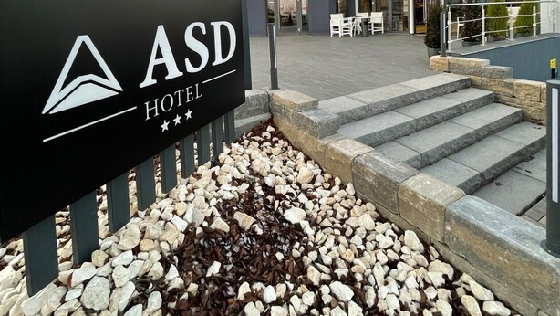 The exterior of the ASD Hotel with a modern design, featuring a prominent entrance and a landscaped area with stepping stones.