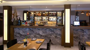 A restaurant with a marble counter, wooden chairs, and a bar area with bottles and glasses.