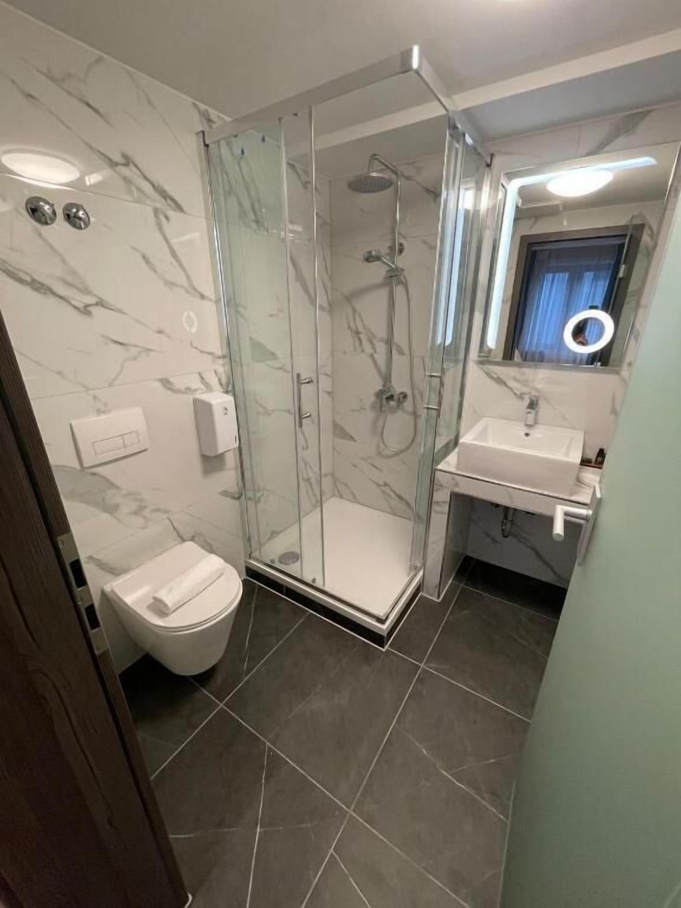 Un baño moderno con ducha envuelta en vidrio, inodoro blanco y lavamanos con espejo superior.