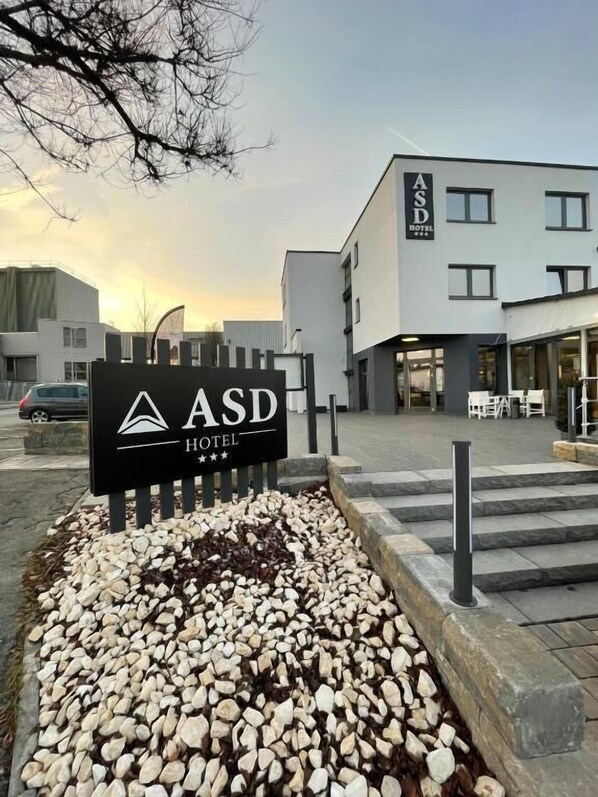 A sign for ASD Hotel with a modern building in the background.