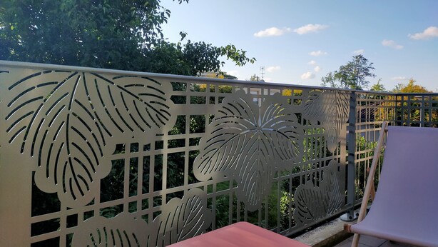 A balcony with a decorative metal fence featuring leaf patterns, a red table, and a white chair. - Beautiful apartment at the gateway to the Medoc (BRUGES)