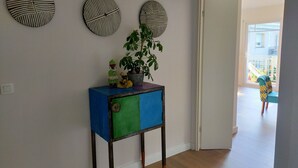 A hallway with a wooden floor, a blue and green cabinet with a potted plant, and three wall-mounted circular decorations. - Beautiful apartment at the gateway to the Medoc (BRUGES)