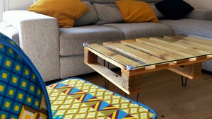 A living room with a grey sofa, two yellow and one black cushion, a wooden coffee table, and a colorful patterned chair. - Beautiful apartment at the gateway to the Medoc (BRUGES)